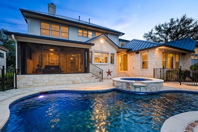 pool at dusk with a sunroom, an in ground hot tub, and a patio area