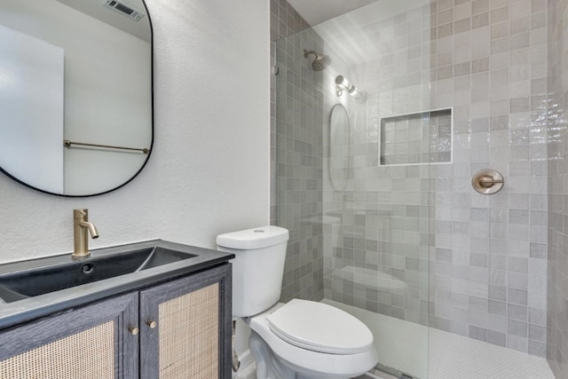 bathroom featuring vanity, a tile shower, and toilet