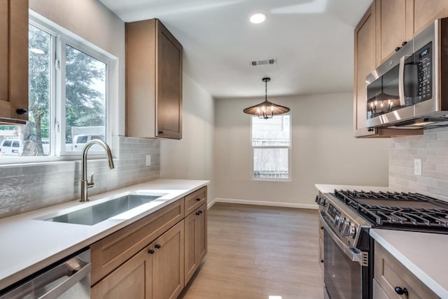 kitchen with stainless steel appliances, backsplash, sink, pendant lighting, and light hardwood / wood-style floors