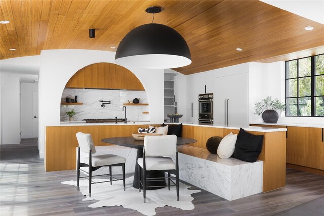 interior space featuring double oven, wood-type flooring, wood ceiling, and backsplash