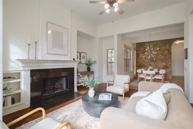 living room featuring a fireplace, dark wood-type flooring, and ceiling fan with notable chandelier