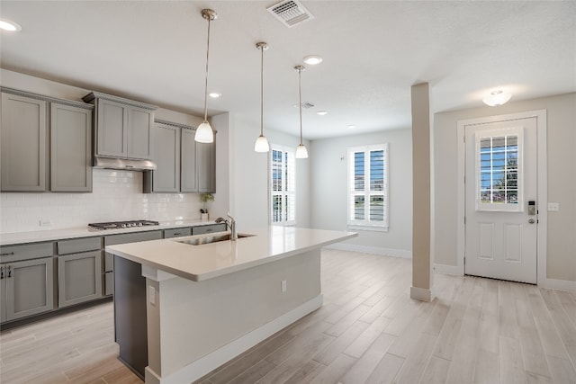 kitchen with light hardwood / wood-style floors, an island with sink, decorative light fixtures, and sink