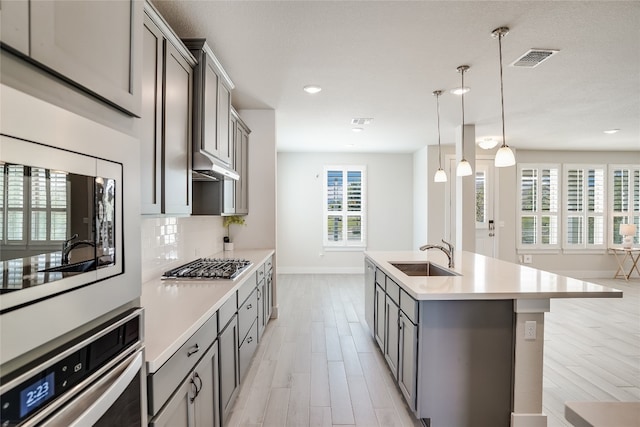 kitchen with pendant lighting, sink, gray cabinetry, stainless steel appliances, and a center island with sink