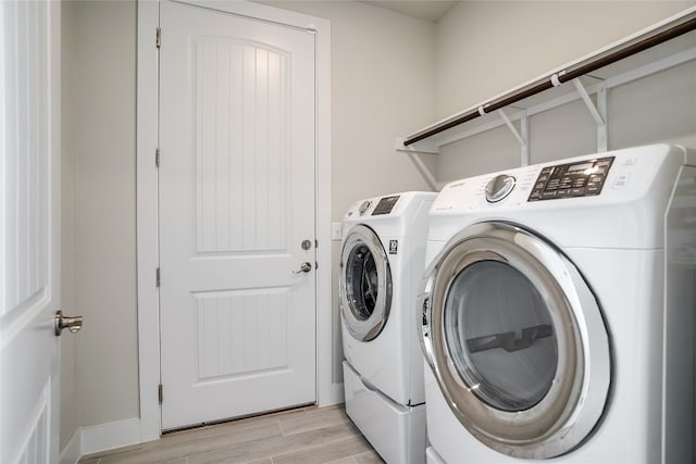 clothes washing area with washing machine and dryer and light hardwood / wood-style flooring