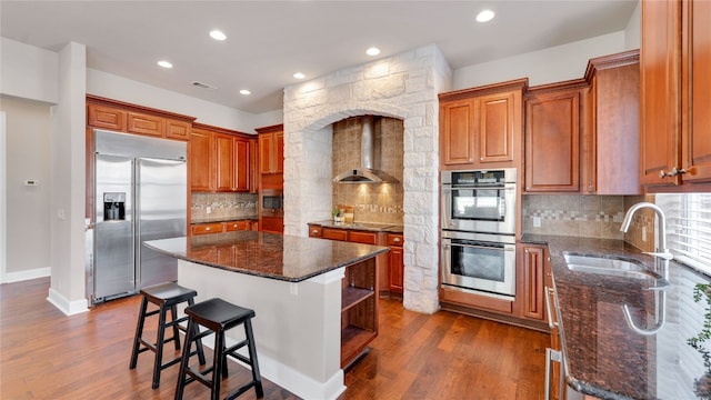 kitchen with sink, a center island, wall chimney exhaust hood, dark wood-type flooring, and appliances with stainless steel finishes