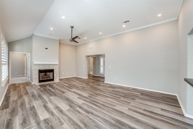 unfurnished living room featuring ceiling fan, a tiled fireplace, light hardwood / wood-style floors, and crown molding