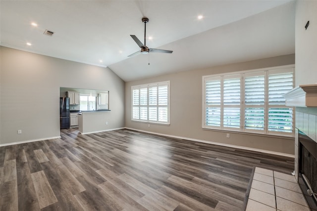 unfurnished living room with a wealth of natural light, vaulted ceiling, ceiling fan, and a tile fireplace