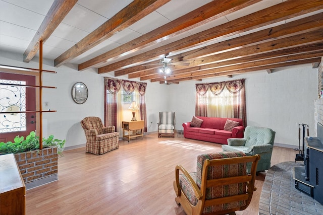 living room with ceiling fan, beam ceiling, wood-type flooring, and a wood stove