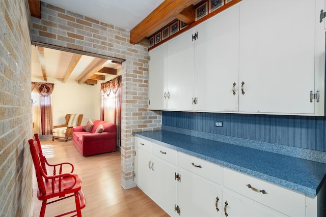 kitchen featuring brick wall, light hardwood / wood-style floors, and white cabinetry