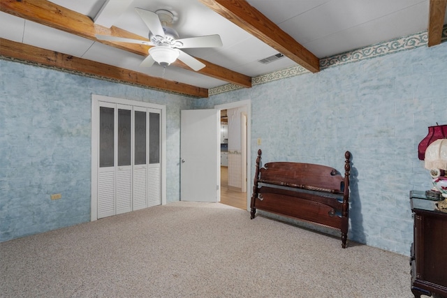 carpeted bedroom with a closet, beam ceiling, and ceiling fan