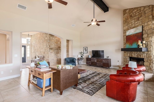 tiled living room with a stone fireplace, beamed ceiling, ceiling fan, and high vaulted ceiling