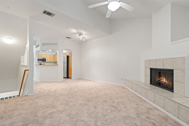 unfurnished living room featuring ceiling fan, light carpet, and a tile fireplace