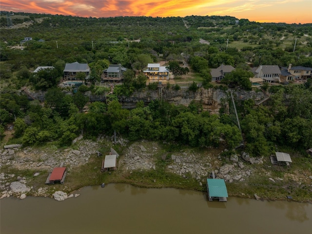 aerial view at dusk featuring a forest view and a water view