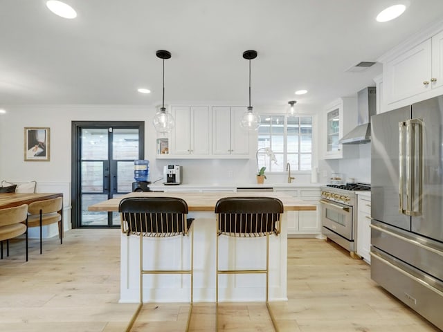 kitchen with wall chimney exhaust hood, white cabinetry, plenty of natural light, and high quality appliances