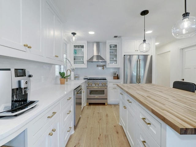 kitchen featuring white cabinetry, wall chimney range hood, wooden counters, and high quality appliances