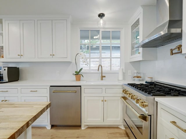 kitchen featuring sink, white cabinetry, wall chimney range hood, appliances with stainless steel finishes, and butcher block countertops