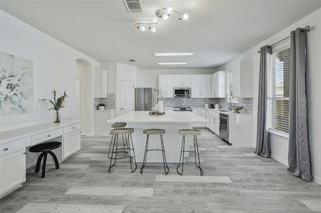 kitchen with white cabinetry, sink, stainless steel appliances, tasteful backsplash, and a kitchen island