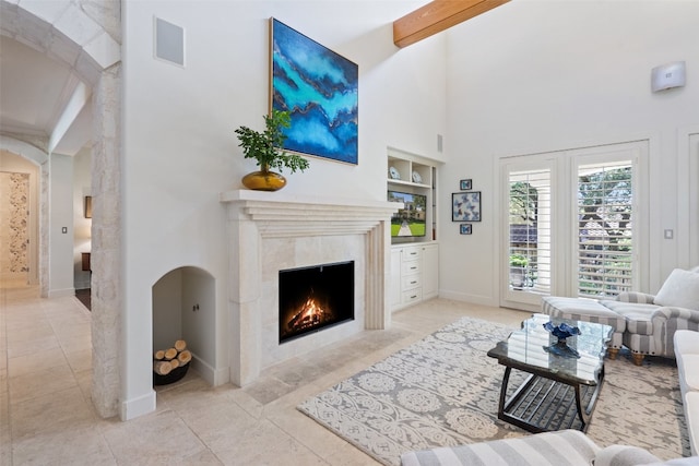 living room with light tile patterned floors, beam ceiling, a high ceiling, and a high end fireplace