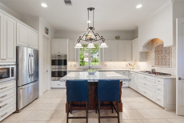 kitchen featuring white cabinets, appliances with stainless steel finishes, ornamental molding, and a kitchen island