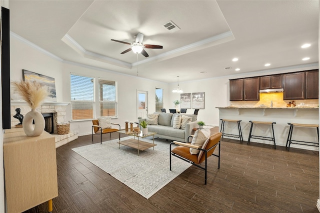 living room featuring dark hardwood / wood-style floors, ceiling fan, a stone fireplace, and a raised ceiling