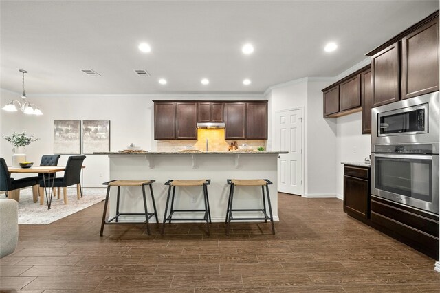 kitchen with pendant lighting, appliances with stainless steel finishes, a center island, tasteful backsplash, and light stone countertops