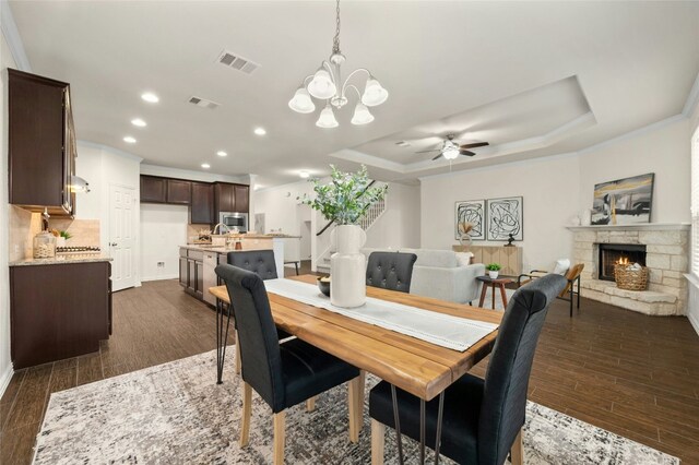 dining room with sink, dark hardwood / wood-style floors, ornamental molding, a stone fireplace, and a raised ceiling