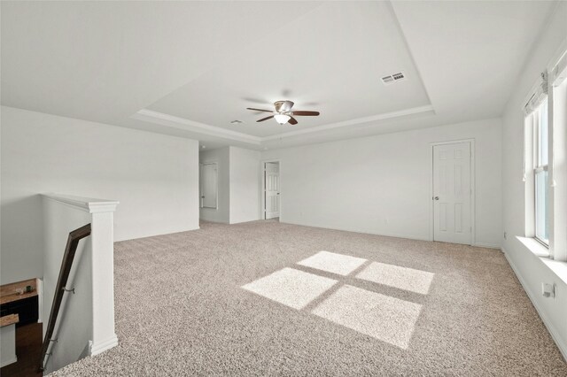 unfurnished living room featuring a raised ceiling, carpet flooring, and a wealth of natural light