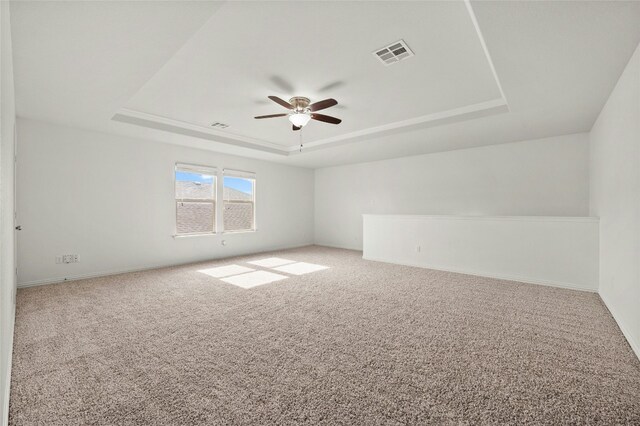 spare room with ceiling fan, a raised ceiling, and carpet