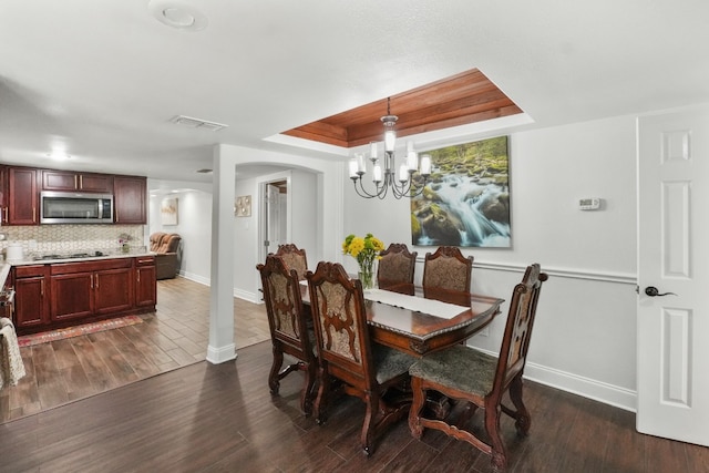 dining room with a raised ceiling, dark hardwood / wood-style flooring, and a chandelier