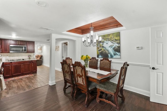 dining area with dark wood-style floors, a raised ceiling, visible vents, arched walkways, and baseboards