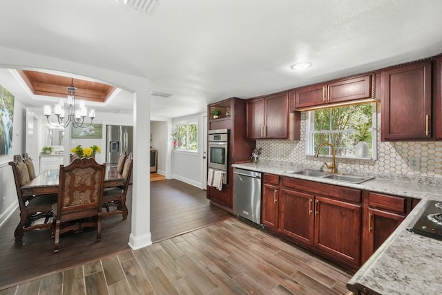 kitchen with sink, hanging light fixtures, a notable chandelier, wood-type flooring, and stainless steel appliances