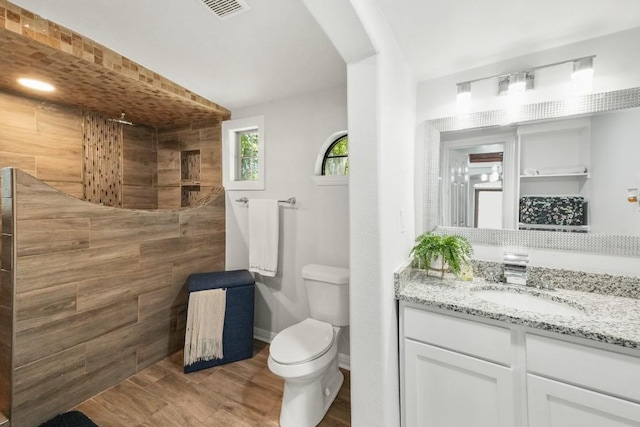 bathroom featuring wood finished floors, vanity, a walk in shower, toilet, and visible vents