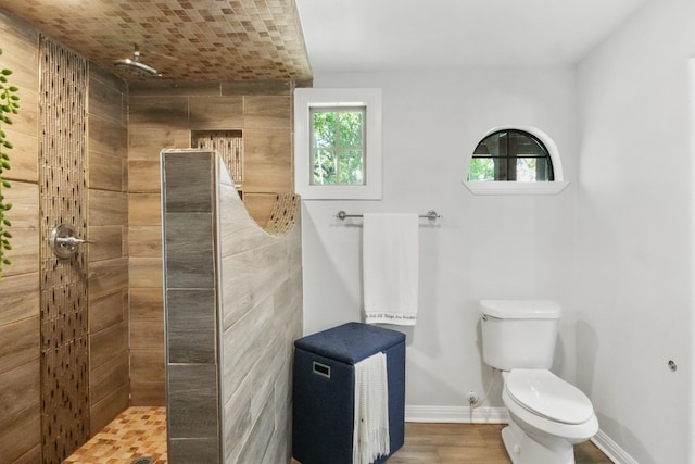 bathroom with a tile shower, toilet, plenty of natural light, and hardwood / wood-style flooring