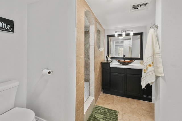 bathroom with tile patterned flooring, a tile shower, vanity, and toilet