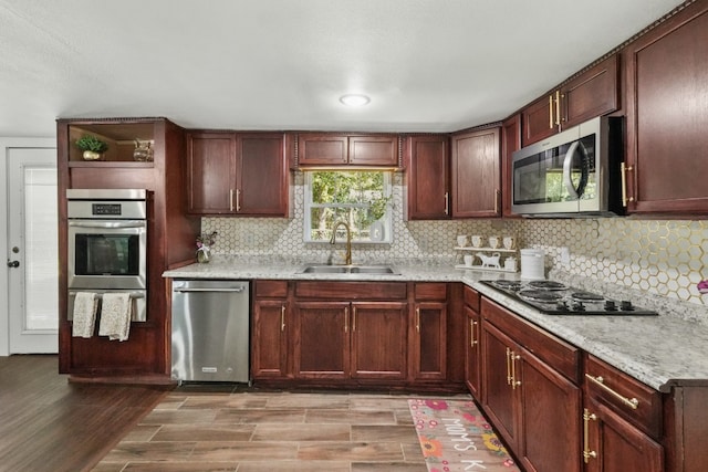 kitchen featuring sink, appliances with stainless steel finishes, tasteful backsplash, light hardwood / wood-style floors, and light stone counters