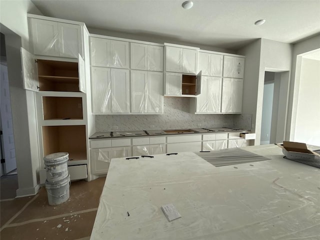 kitchen featuring concrete flooring, stovetop, tasteful backsplash, and white cabinetry