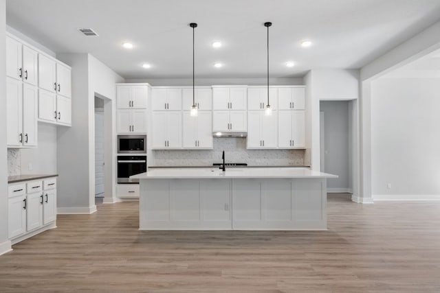 4804 Destination Way, Jonestown, TX 78645 - kitchen with built in microwave, black oven, under cabinet range hood, backsplash, and light wood-style flooring