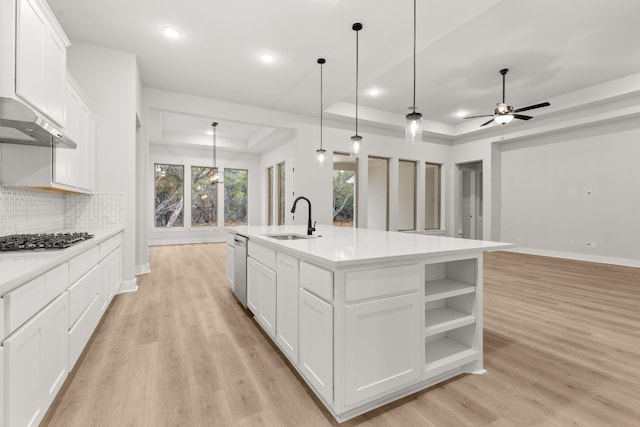 kitchen with sink, appliances with stainless steel finishes, white cabinets, a center island with sink, and a raised ceiling