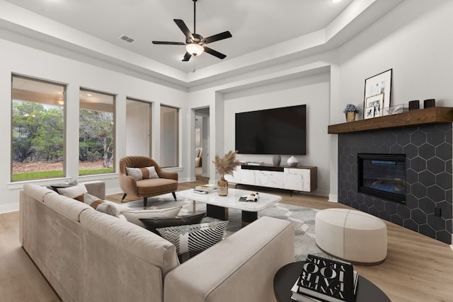 living room with a raised ceiling, ceiling fan, and light wood-type flooring