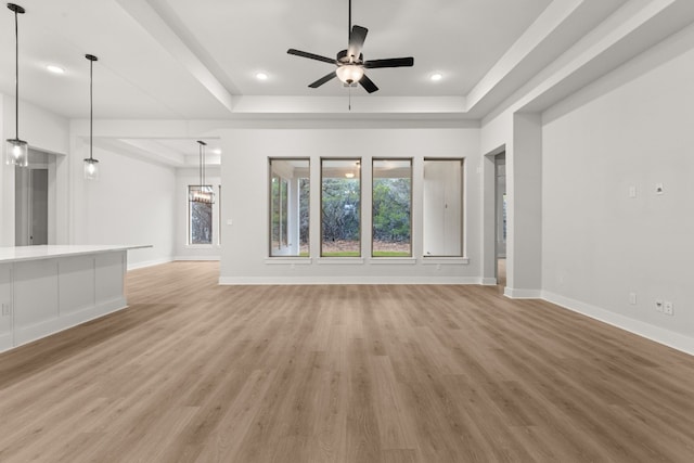 unfurnished living room featuring ceiling fan, a raised ceiling, and light wood-type flooring