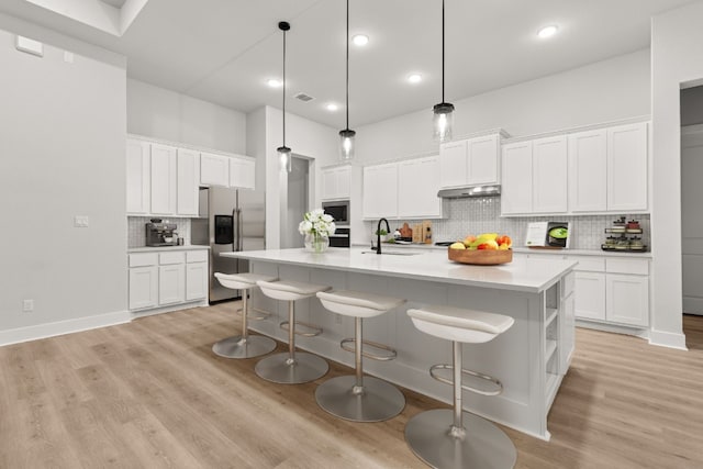 kitchen with stainless steel appliances, white cabinetry, and a center island with sink