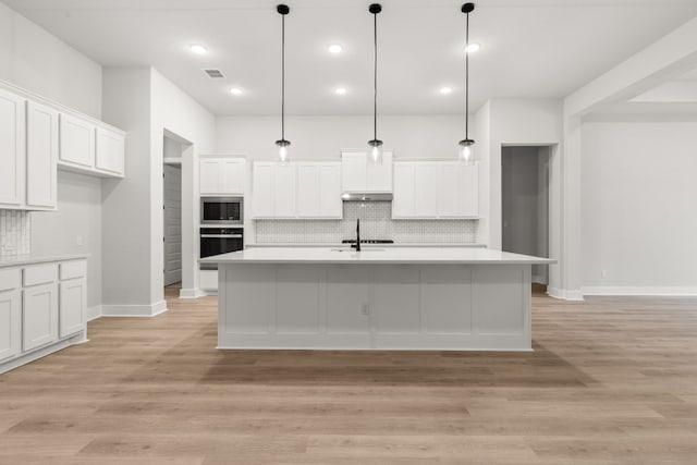 kitchen featuring white cabinets, a kitchen island with sink, pendant lighting, and black oven