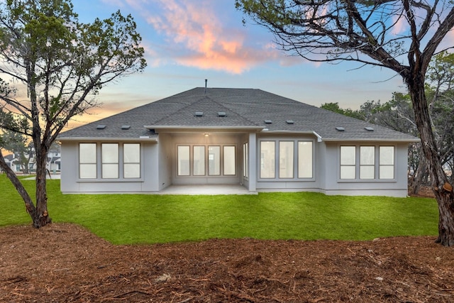 back house at dusk with a patio area and a lawn