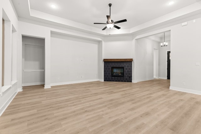 unfurnished living room with a fireplace, a raised ceiling, ceiling fan with notable chandelier, and light hardwood / wood-style flooring