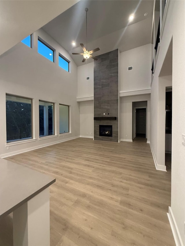 unfurnished living room with a towering ceiling, a tile fireplace, light hardwood / wood-style floors, and ceiling fan