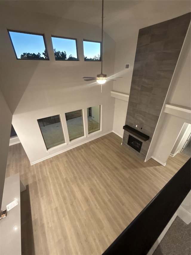 unfurnished living room with hardwood / wood-style floors, a tile fireplace, and ceiling fan