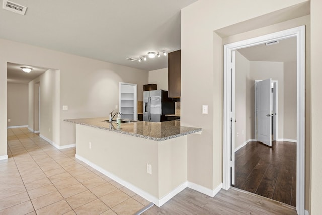 kitchen featuring light wood-type flooring, light stone counters, sink, kitchen peninsula, and stainless steel fridge