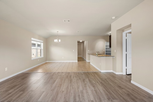 empty room with an inviting chandelier, light wood-type flooring, lofted ceiling, and sink