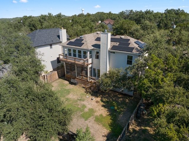 back of house with a chimney, solar panels, a sunroom, roof with shingles, and a fenced backyard