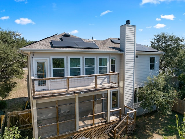 rear view of property featuring a balcony, a deck, and solar panels